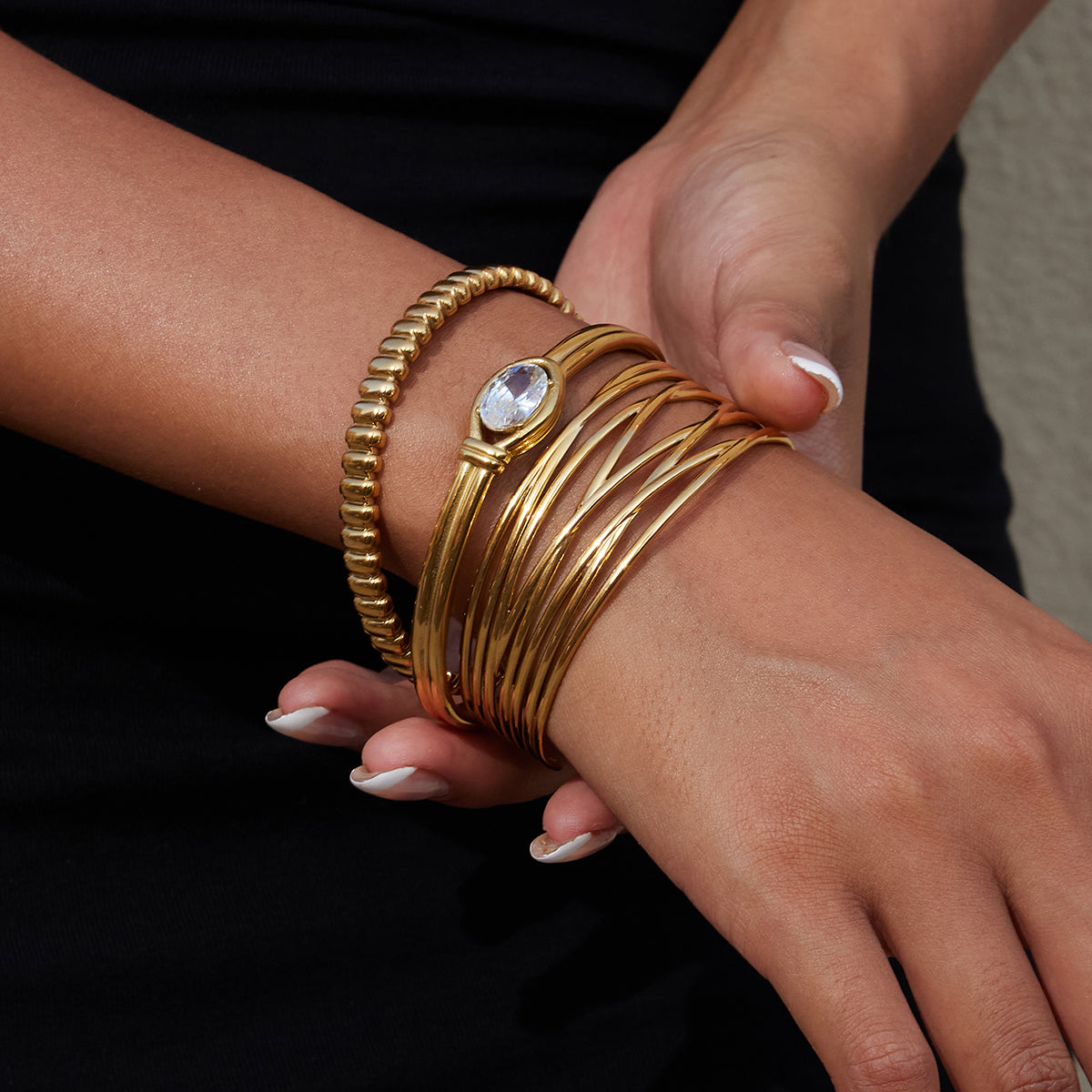 Close-up of a wrist wearing multiple gold bracelets with a clear gemstone on a dark background