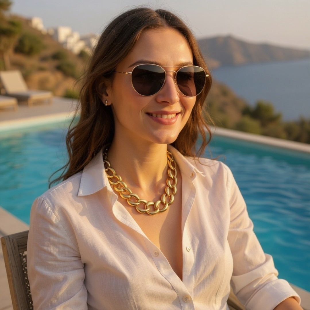 Woman wearing sunglasses and a gold necklace by a pool with a scenic background