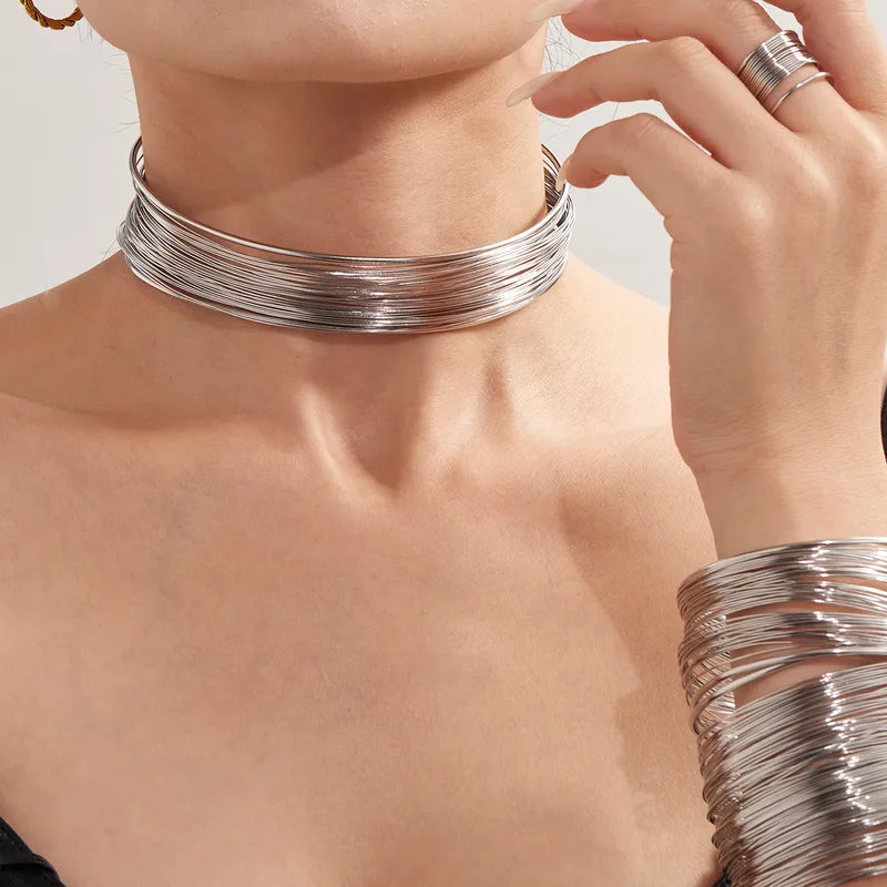 Close-up of a person wearing a silver choker and bracelet on a neutral background