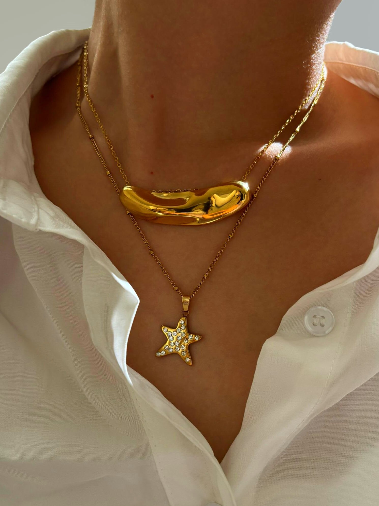 Close-up of a person wearing two gold necklaces, one with a star pendant and the other with a unique design.Α – Χονδρική So Cute by Dimi