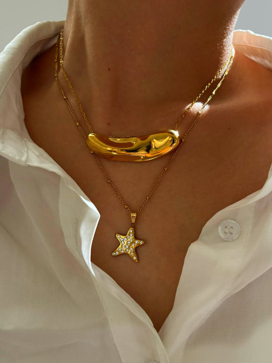 Close-up of a person wearing two gold necklaces, one with a star pendant and the other with a unique design.Α – Χονδρική So Cute by Dimi