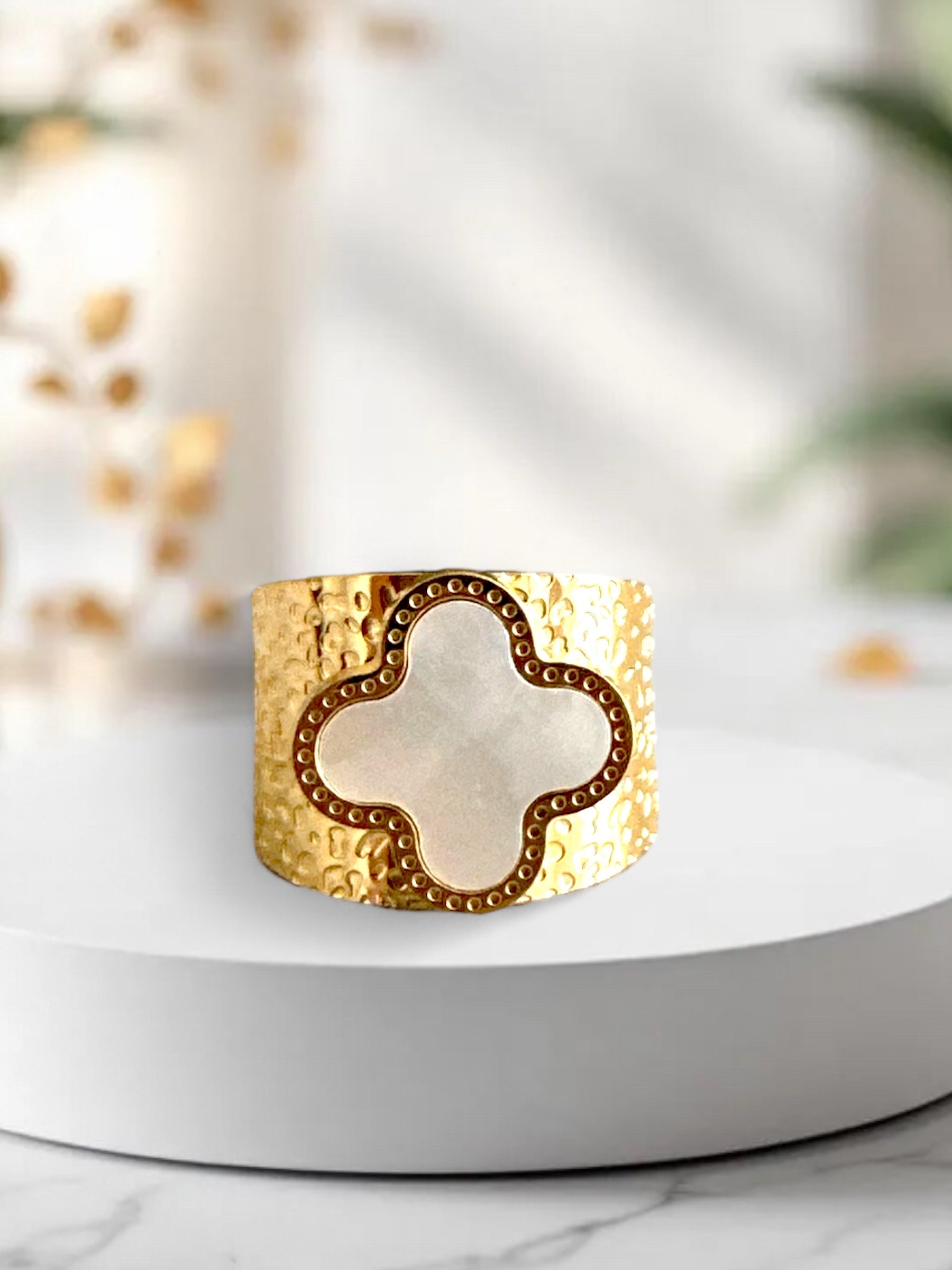 Gold hammered adjustable ring with white clover-shaped mother of pearl on white background, perfect for boho-chic styling.