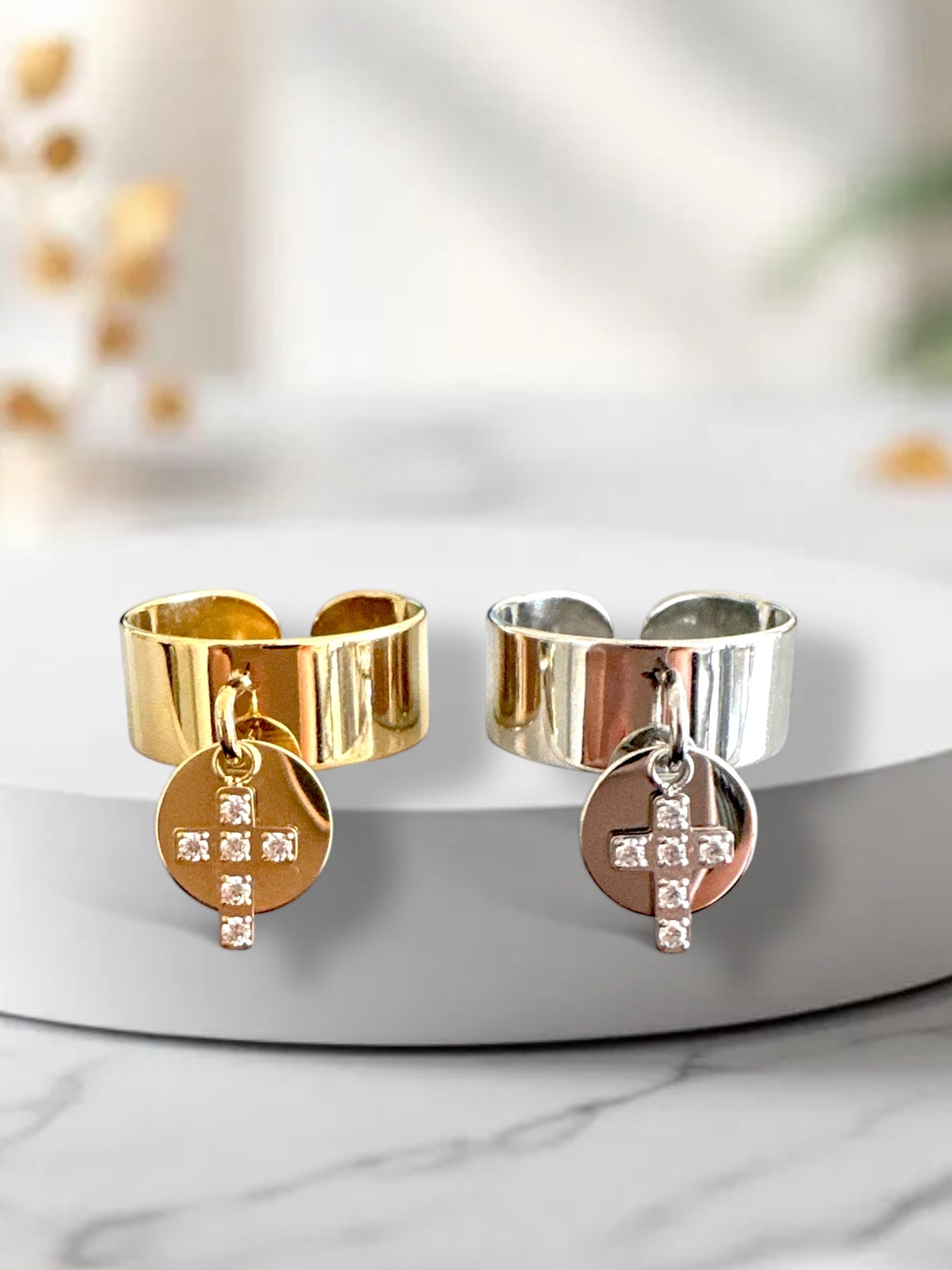 Ατσάλινα δαχτυλίδια σε χρυσό και ασημί με κρεμαστό σταυρό διακοσμημένο με στρας, σε λευκό φόντο.