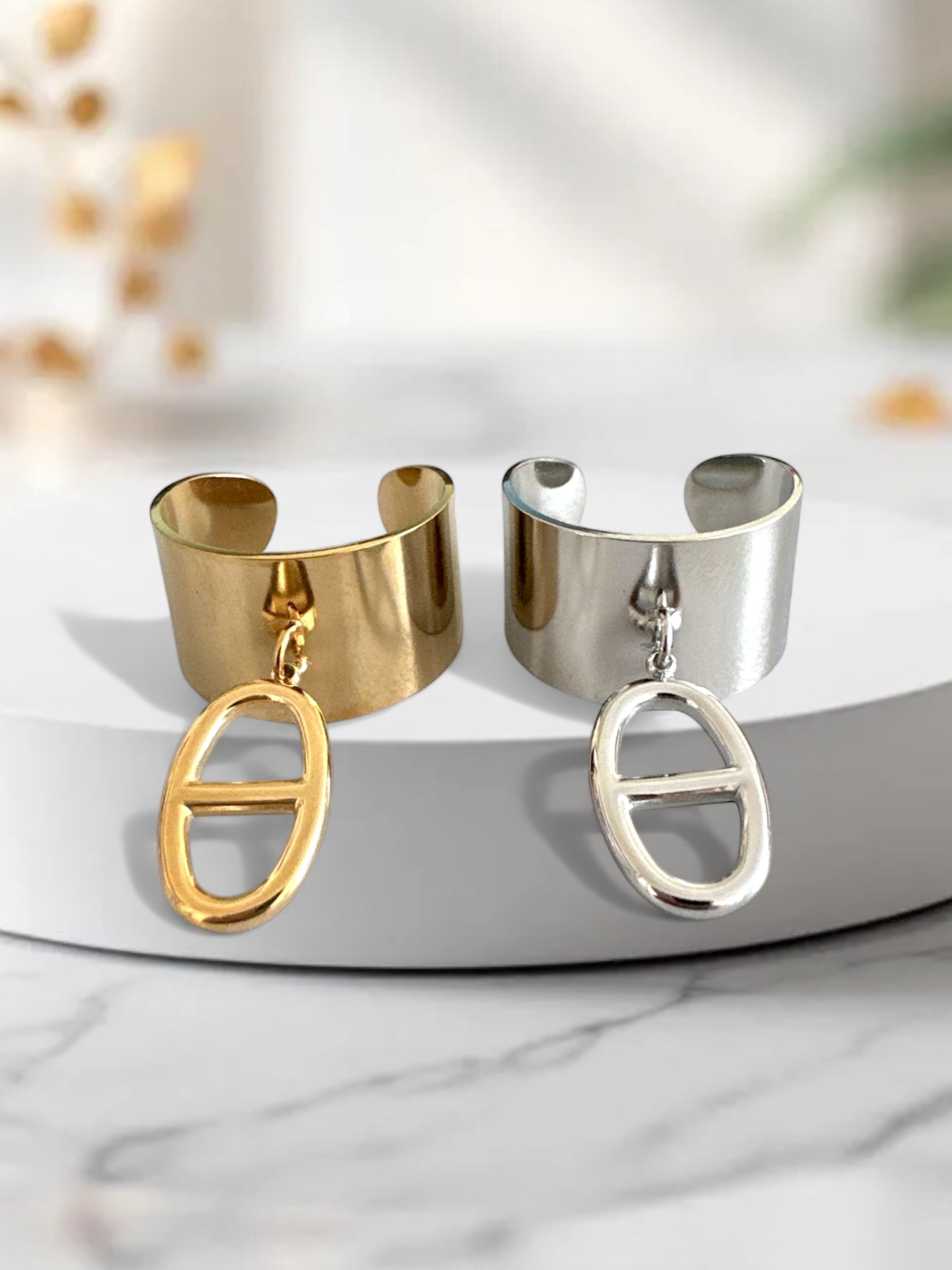 Δύο ατσάλινα δαχτυλίδια, ένα χρυσό και ένα ασημί, με οβάλ charm, σε λευκή μαρμάρινη βάση