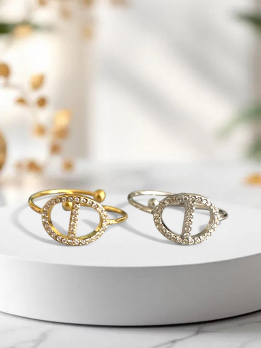 Ατσάλινα δαχτυλίδια σε χρυσό και ασημί με διακοσμητικό μοτίβο σε σχήμα D στολισμένο με στρας, σε λευκό φόντο.