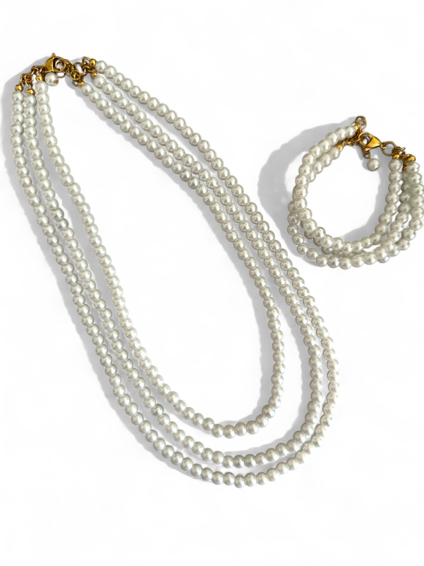 Τριπλό κολιέ και βραχιολι με γυάλινες περλέ χάντρες σε διαβαθμισμένα μήκη και ατσάλινο κούμπωμα, σε λευκό φόντο.