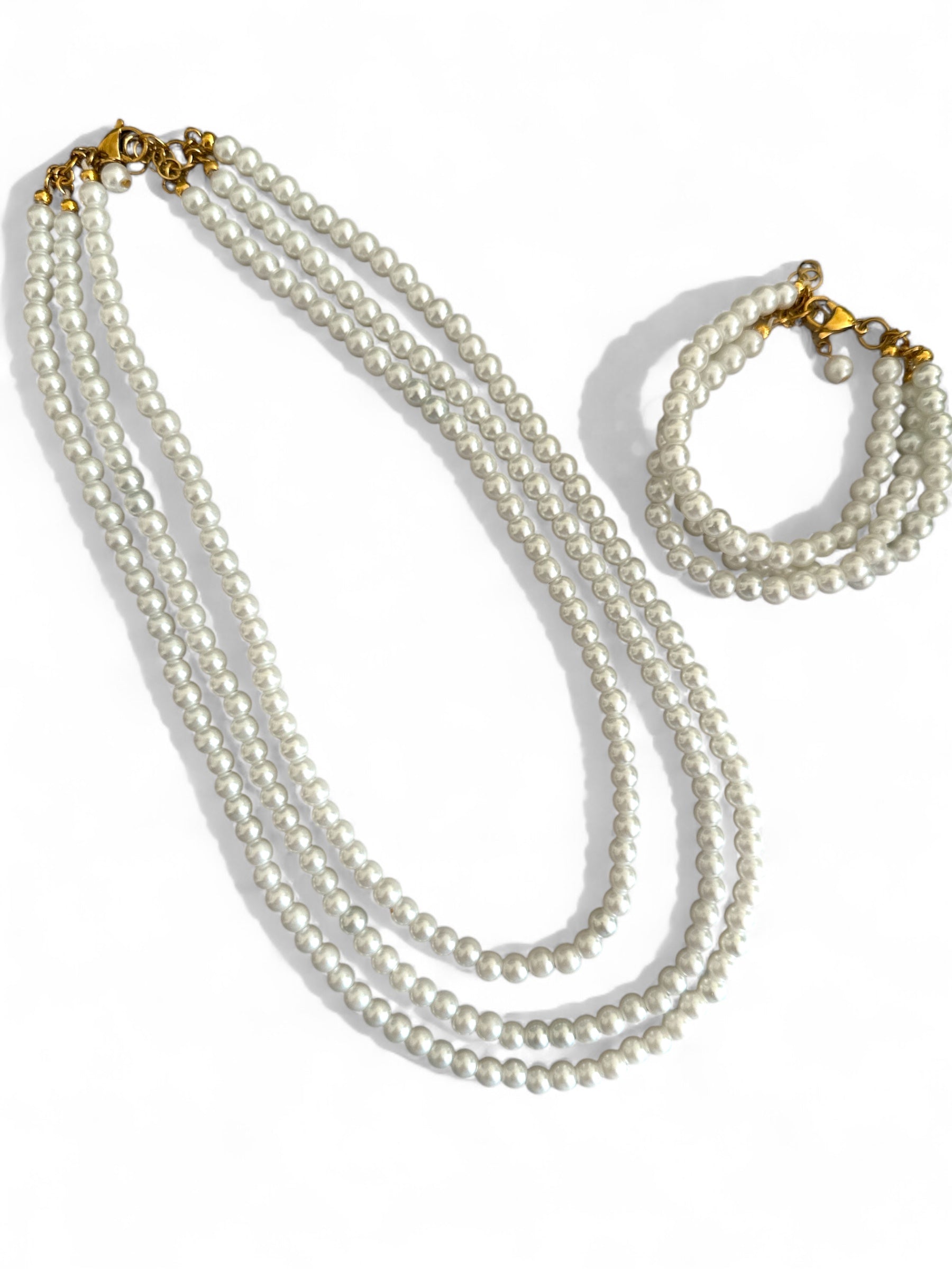Τριπλό κολιέ και βραχιολι με γυάλινες περλέ χάντρες σε διαβαθμισμένα μήκη και ατσάλινο κούμπωμα, σε λευκό φόντο.