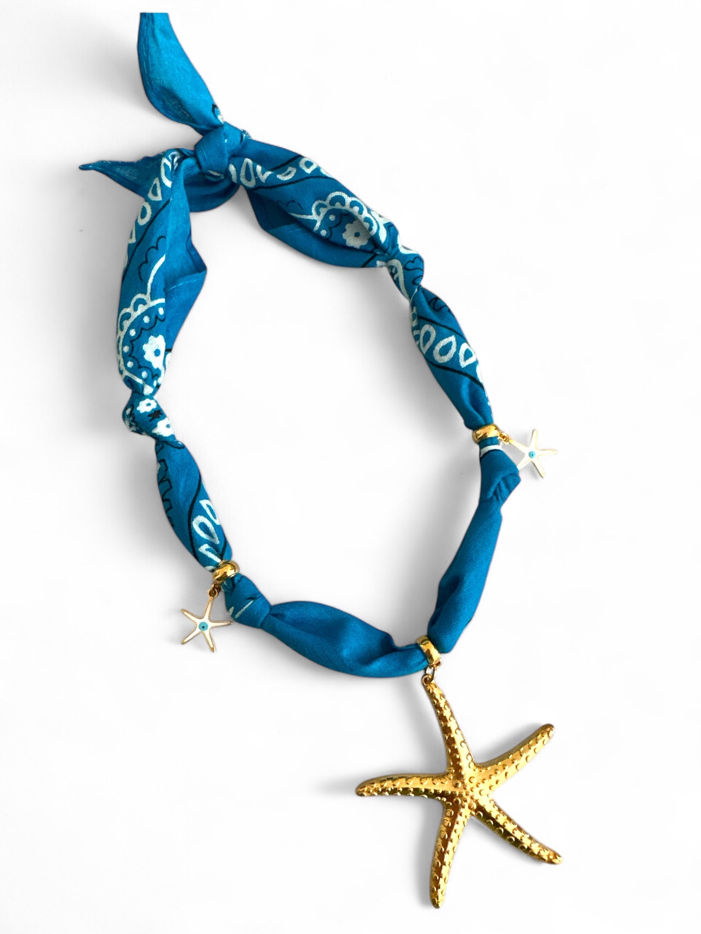 Blue bandana necklace with white patterns and a gold starfish charm on a white background