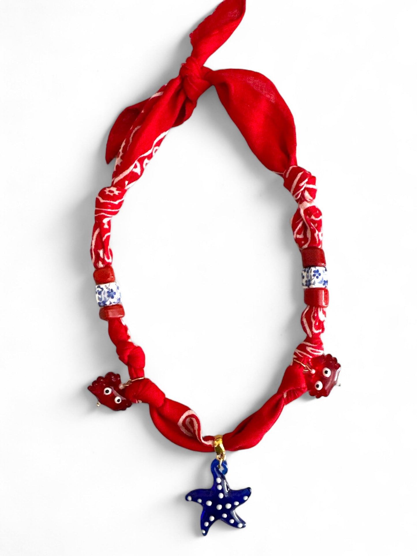 Necklace with red bandana, star-shaped blue pendant, and white beads on a white background
