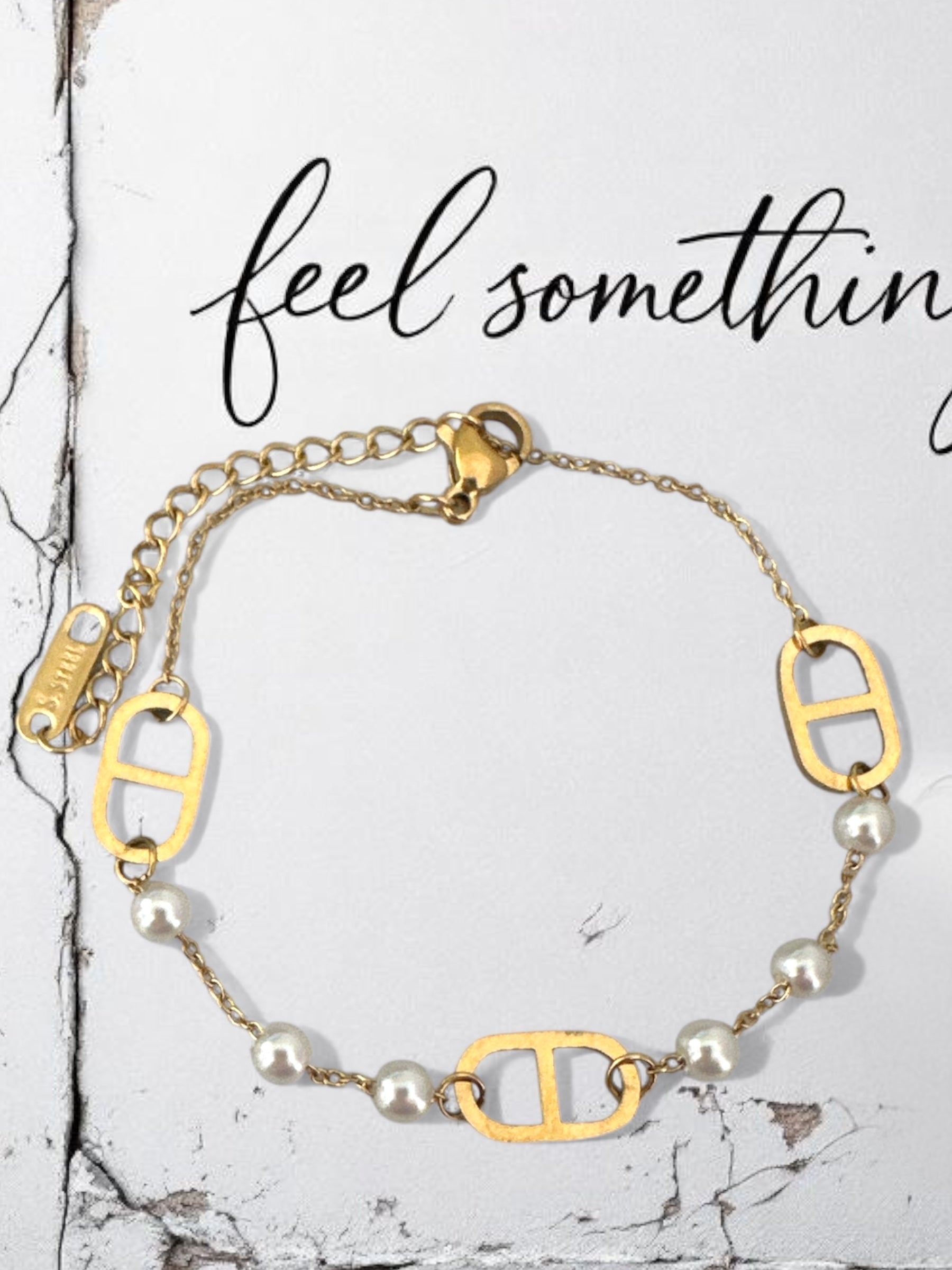 Gold bracelet with pearl beads on a marble surface, text 'feel something' above.
