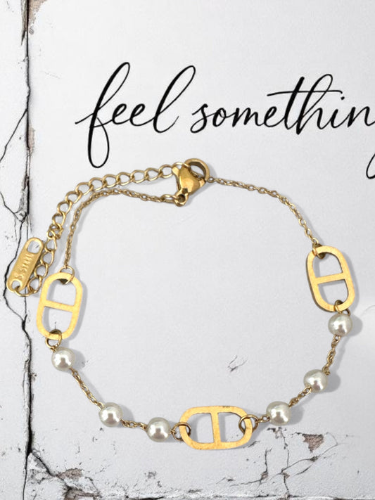 Gold bracelet with pearl beads on a marble surface, text 'feel something' above.
