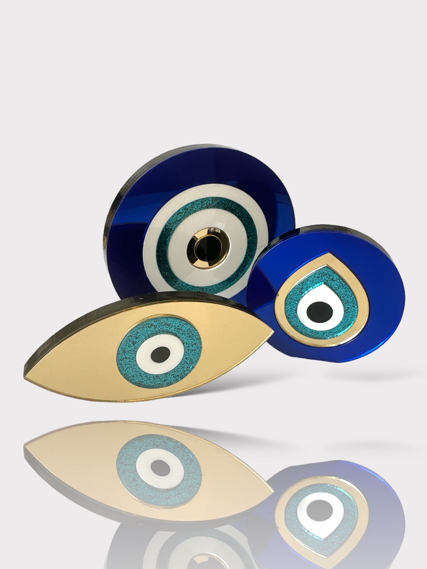 Τρία επιτραπέζια γούρια από plexiglass σε στρογγυλό, οβάλ και δάκρυ σχήμα, σε μπλε, λευκό, τιρκουάζ και χρυσό.