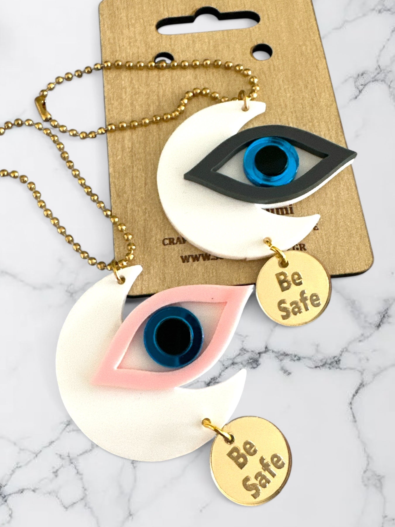 Γούρια αυτοκινήτου σε σχήμα μισοφέγγαρου με μάτι σε ροζ και γκρι πλέξιγκλας, μπλε διάφανο κέντρο και μεταλλικό charm “Be Safe”