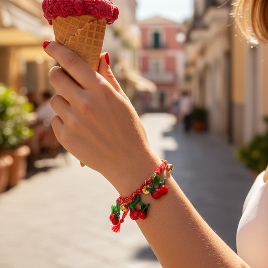 Hand holding a red ice cream cone with a cherry bracelet on a street background