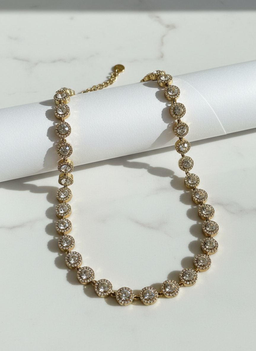Gold necklace with clear zircon stones and rhinestones on a white marble surface