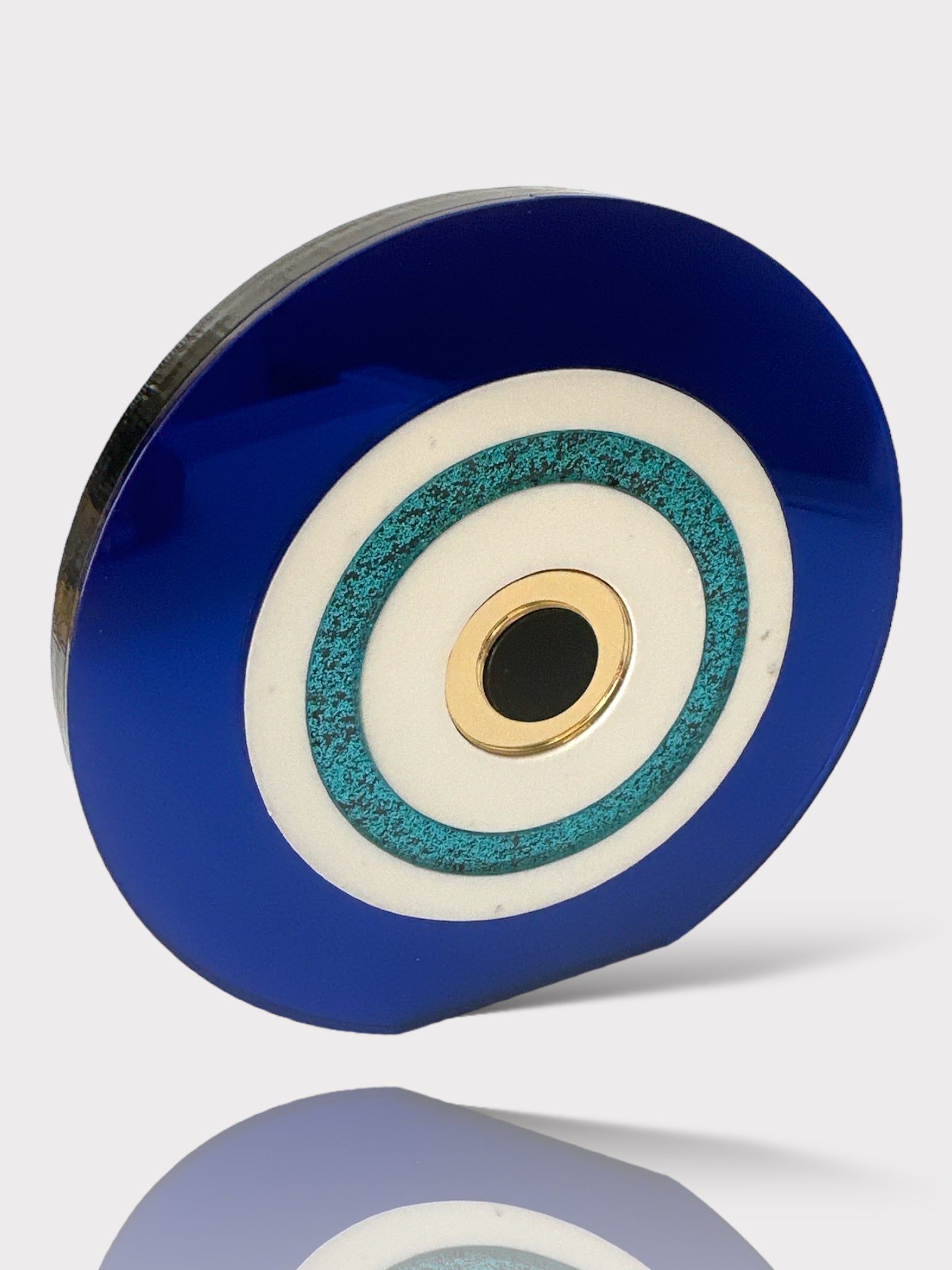 Επιτραπέζιο γούρι μάτι από μπλε και λευκό plexiglass με τιρκουάζ glitter λεπτομέρεια και χρυσό κέντρο σε λευκό φόντο.